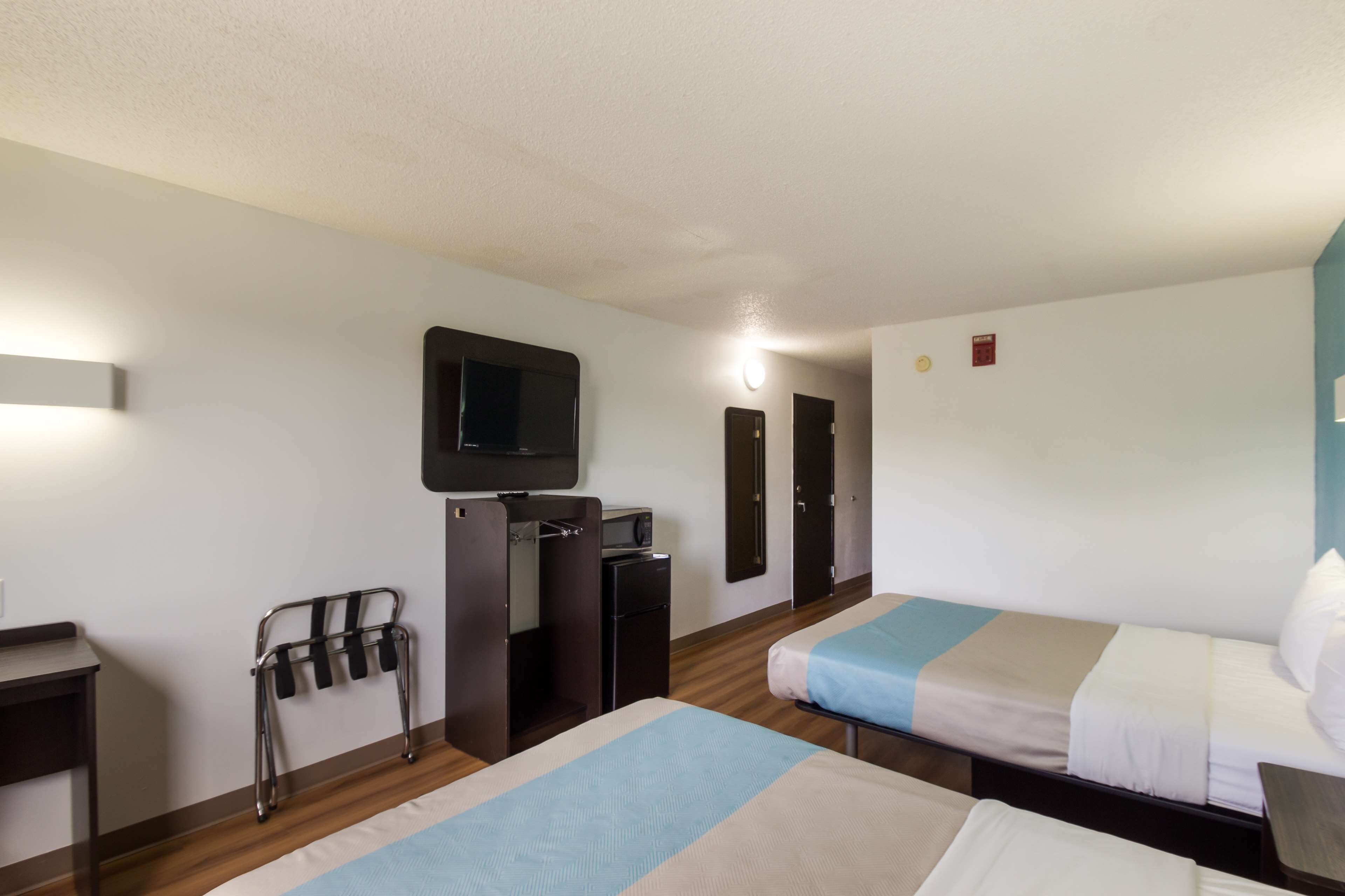 Quarto de hotel com duas camas, uma escrivaninha, televisão e uma pequena cozinha.