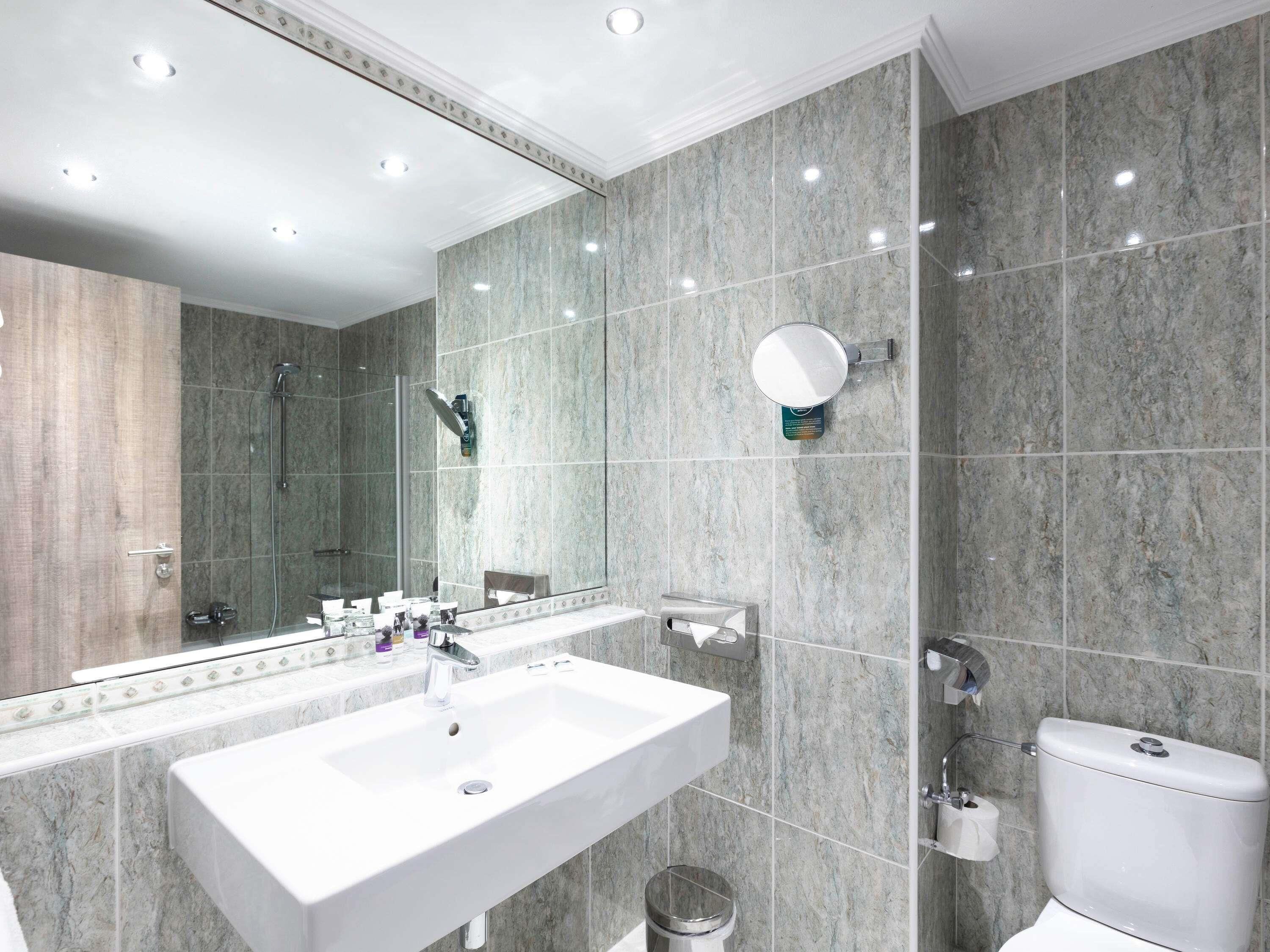 Een moderne badkamer met een grote spiegel, twee wastafels, een douche en een toilet.