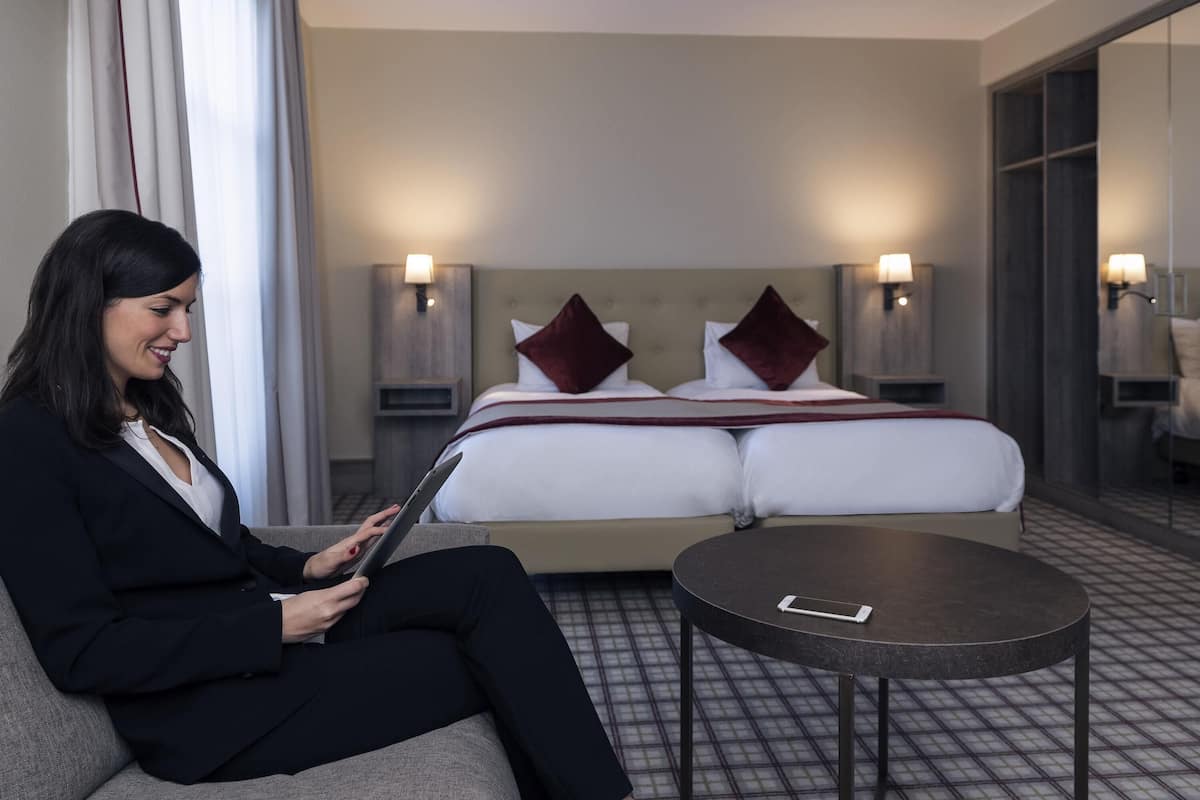 A hotel room with a bed, bedside tables, a round table, and a person using a tablet.