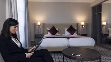 Una habitación de hotel con cama, mesitas de noche, una mesa redonda y una persona usando una tablet.
