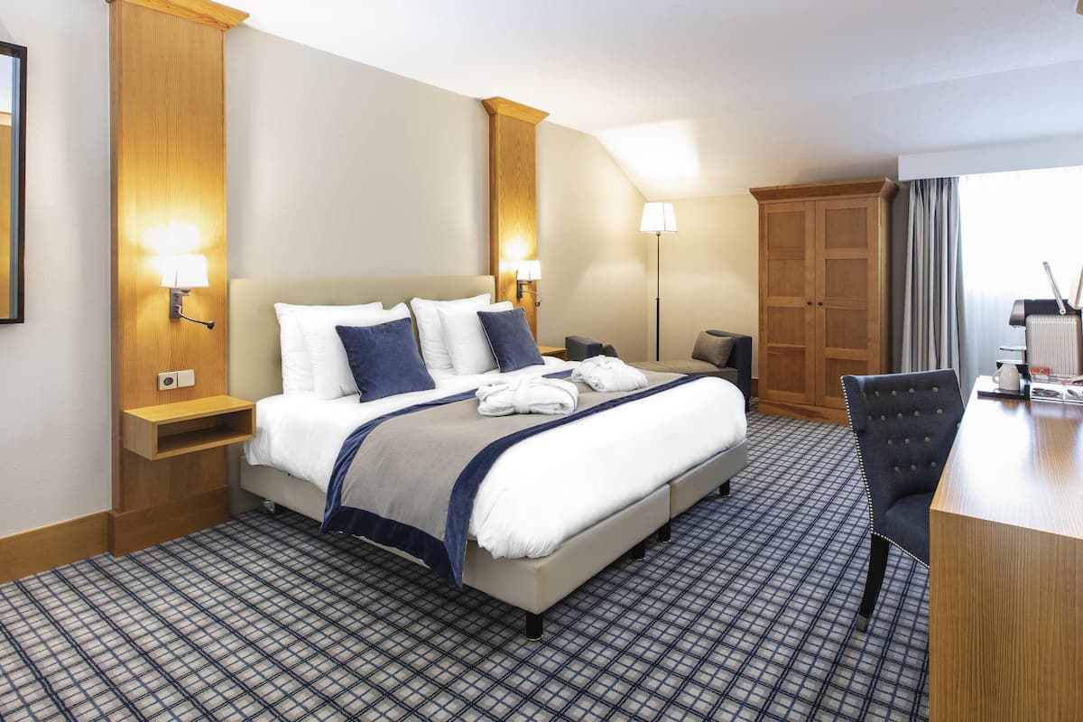 A hotel room with a large bed, bedside tables, a desk, and a wardrobe.