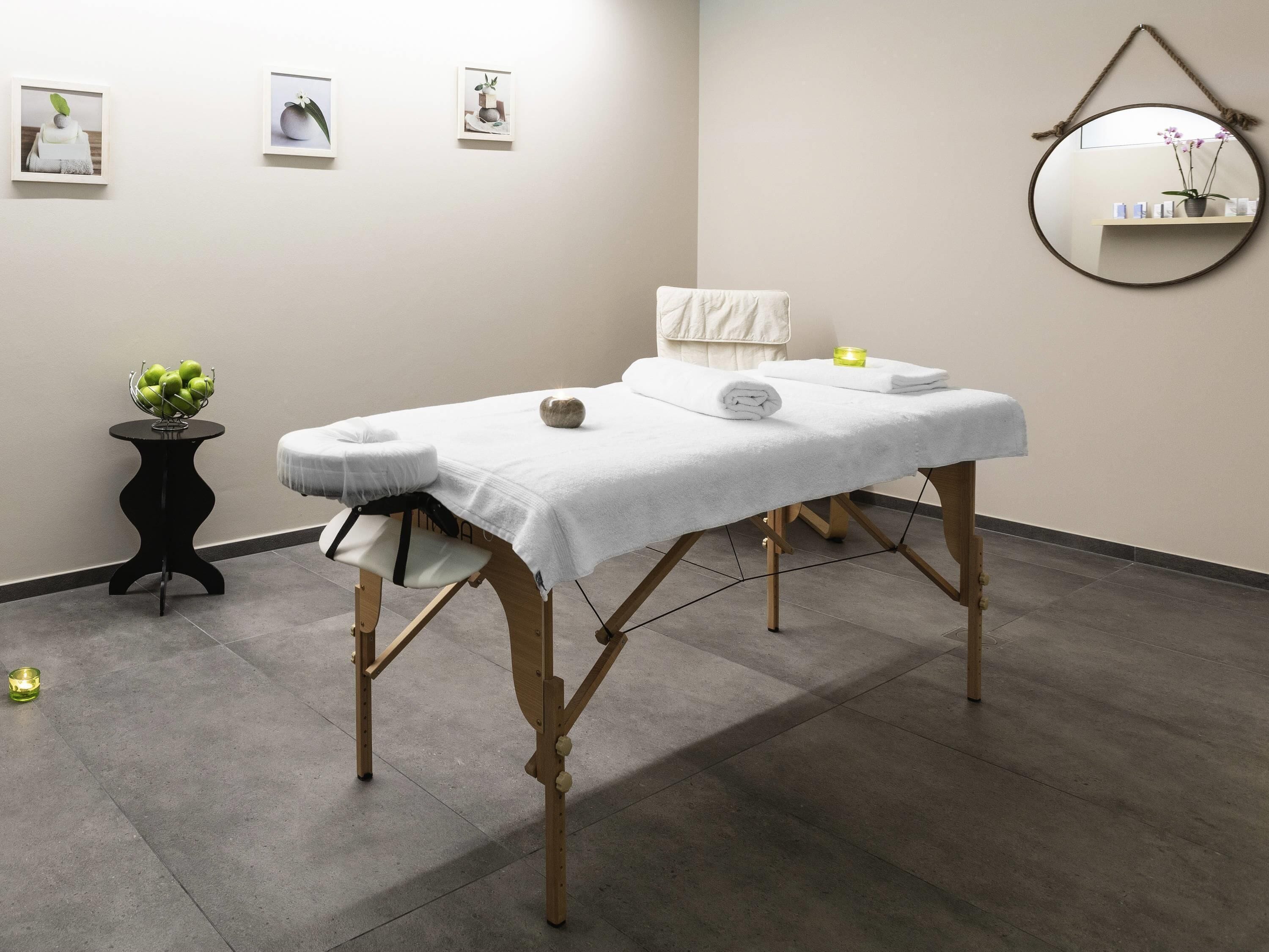 A massage table with a white towel, a small plant, and a candle on a black side table.
