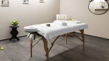 A massage table with a white towel, a small plant, and a candle on a black side table.