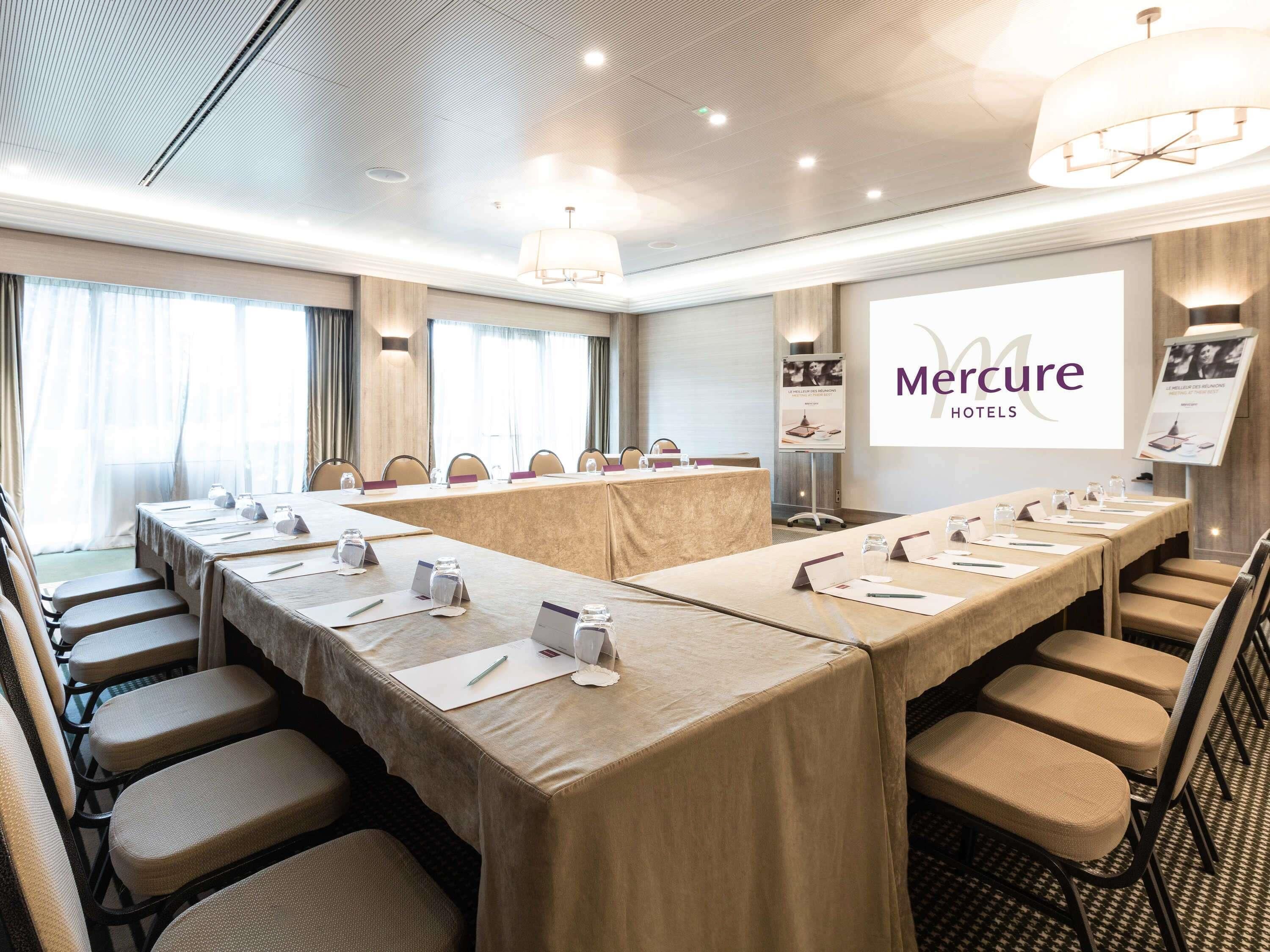 Une salle de conférence équipée d’une longue table, de chaises, de plaques nominatives et d’un écran de présentation affichant le logo « Mercure Hotels ».