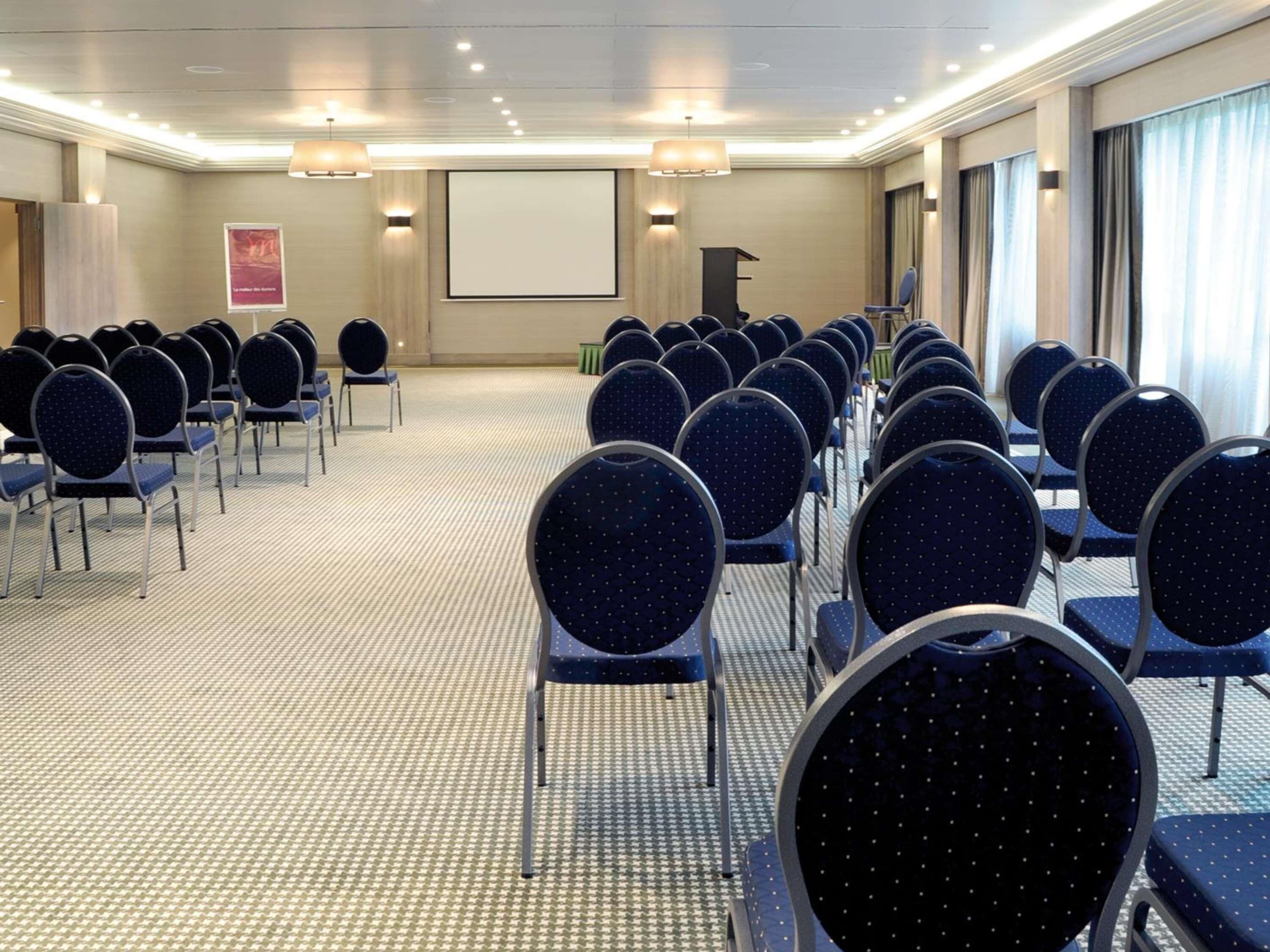 A conference room with rows of chairs, a podium, a screen, and a carpeted floor.