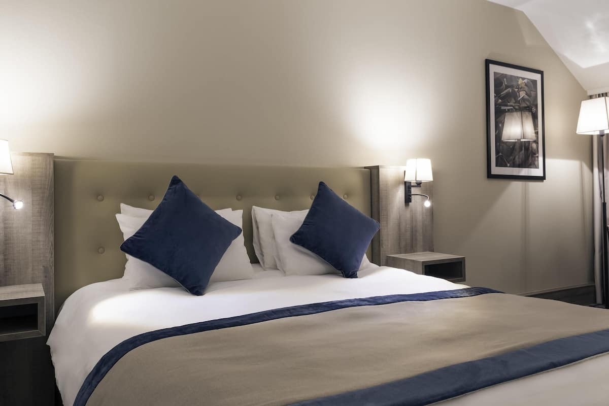 A hotel room with a large bed, two bedside lamps, a framed picture on the wall, and a nightstand with a lamp.