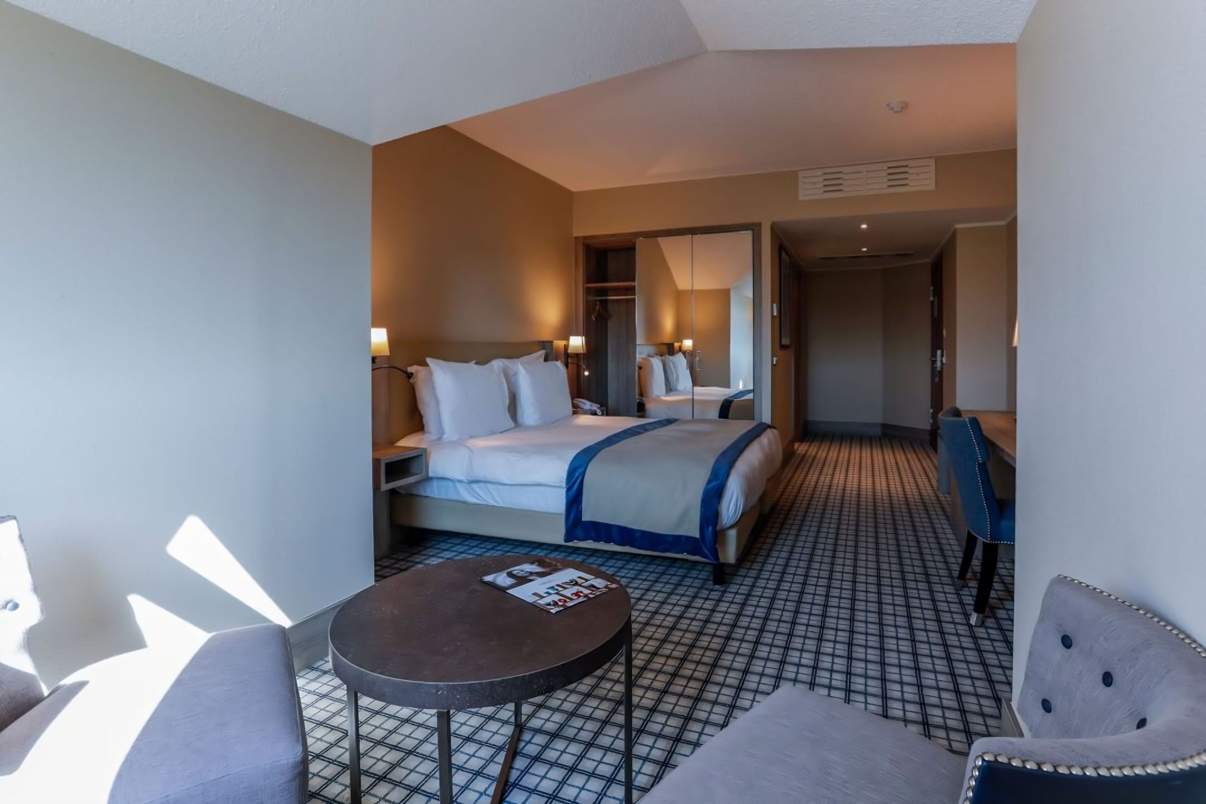Habitació d'hotel amb un llit, una taula petita i una cadira. Hi ha un mirall i un armari.