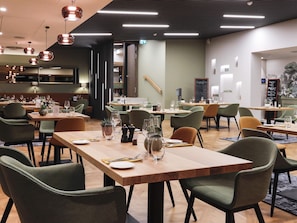 Ein modernes Restaurant mit mehreren Esstischen, Stühlen und hängenden Pendelleuchten.
