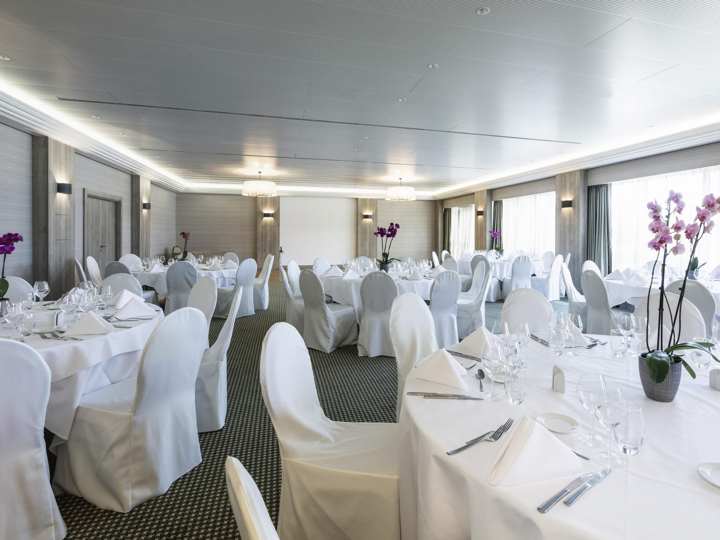 A conference room with round tables, white chairs, and floral centerpieces.