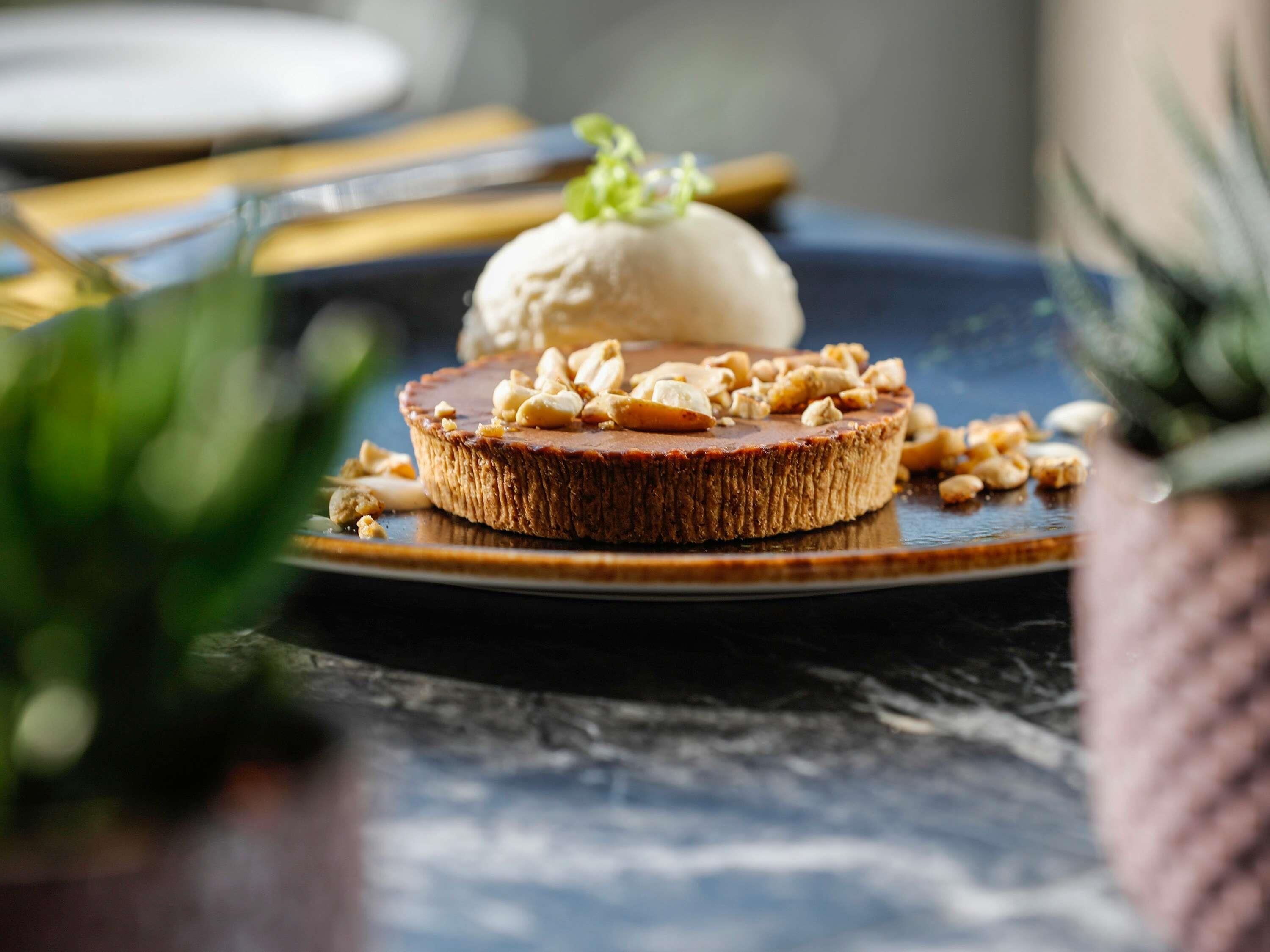 Un plato de postre con una rebanada de pastel cubierta de nueces y una bola de helado.