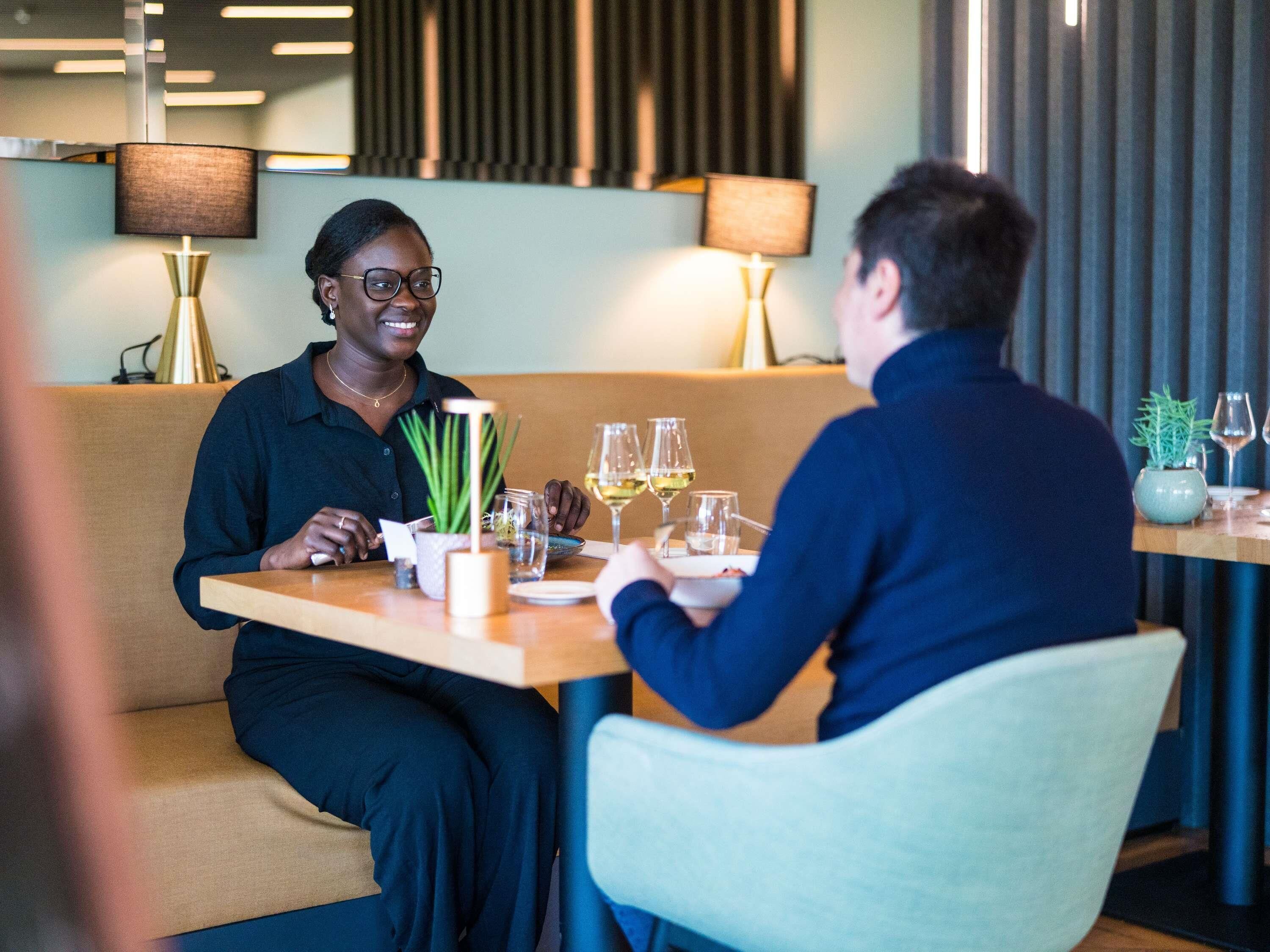 A dining area with a table set for two, featuring a plant, wine glasses, and a menu.