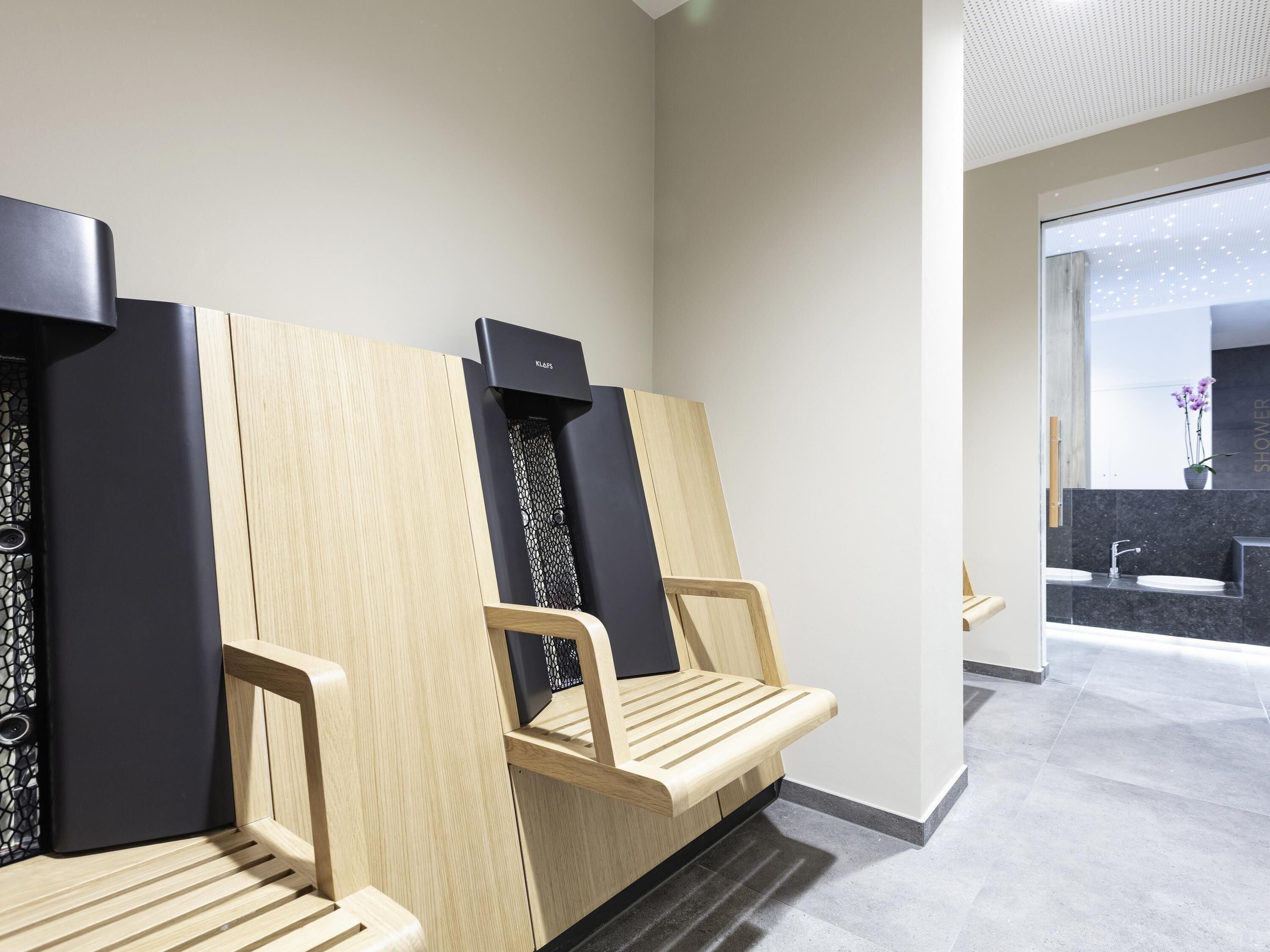 Un baño moderno con bancos de madera y accesorios negros, una zona de ducha con encimera de mármol y un amplio ventanal que proporciona luz natural.