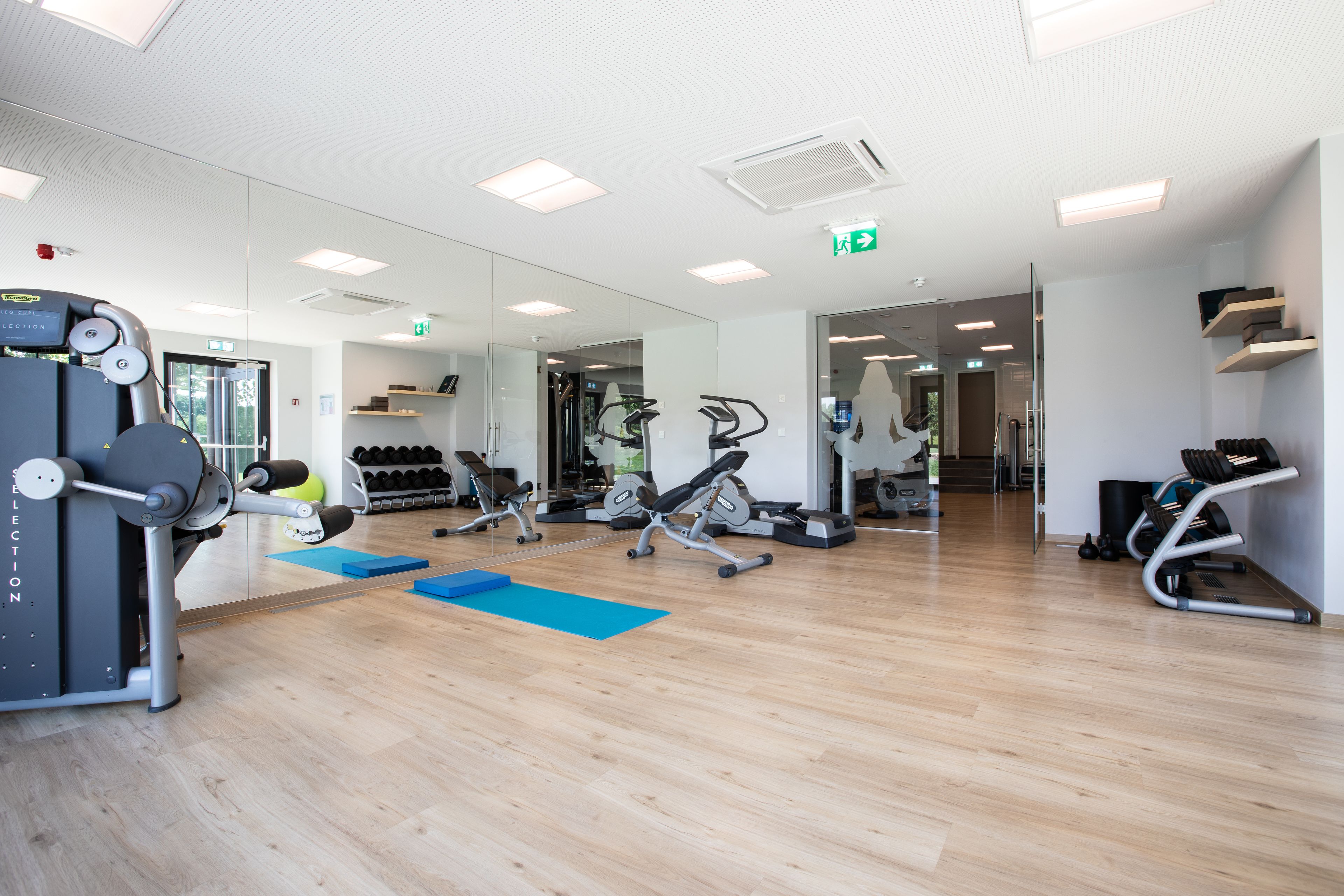 Un gimnasio moderno con diverso equipamiento de ejercicio, una colchoneta azul y piso de madera.