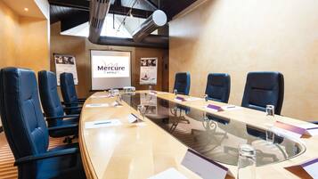 Une salle de conférence avec une longue table, des chaises bleues, un écran de projection et un panneau indiquant « Hôtels Mercure ».