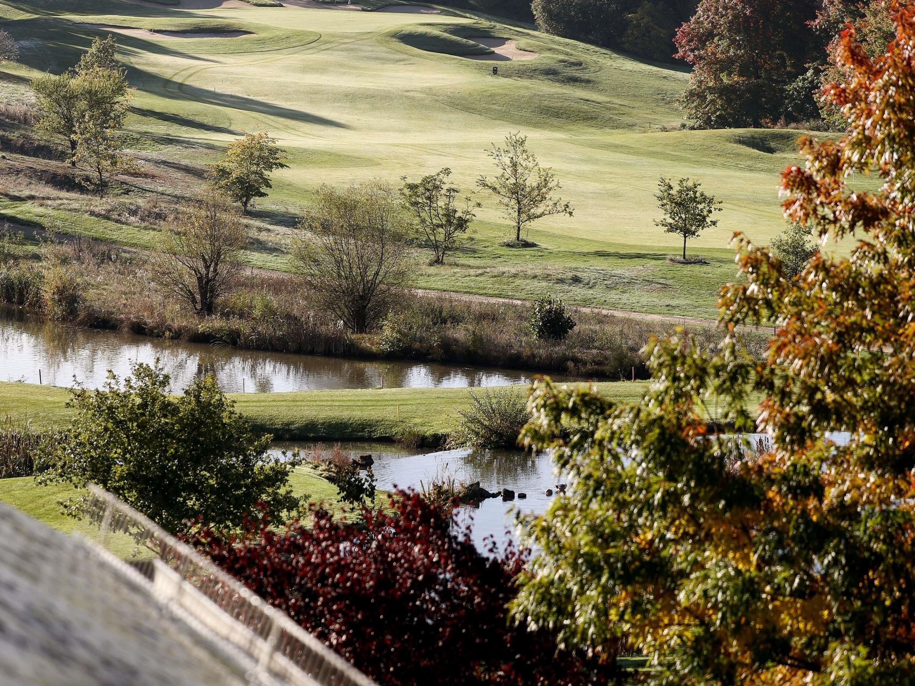 Een golfbaan met een vijver, bomen en een hek.