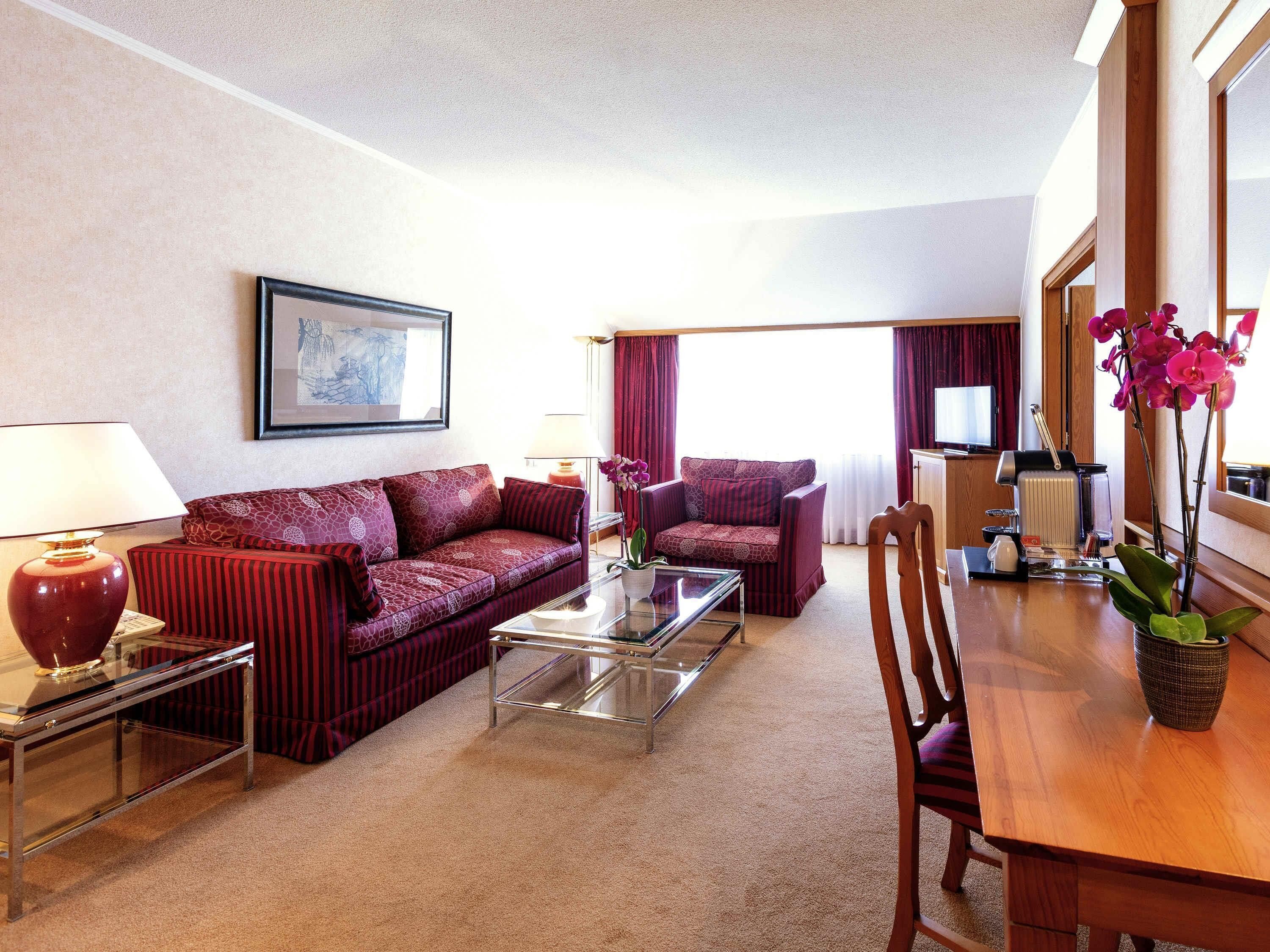 Een hotelkamer met een bank, fauteuil, salontafel, eettafel en een koffieapparaat.