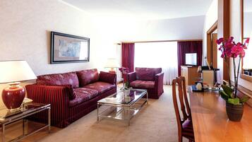 Een hotelkamer met een bank, fauteuil, salontafel, eettafel en een koffieapparaat.