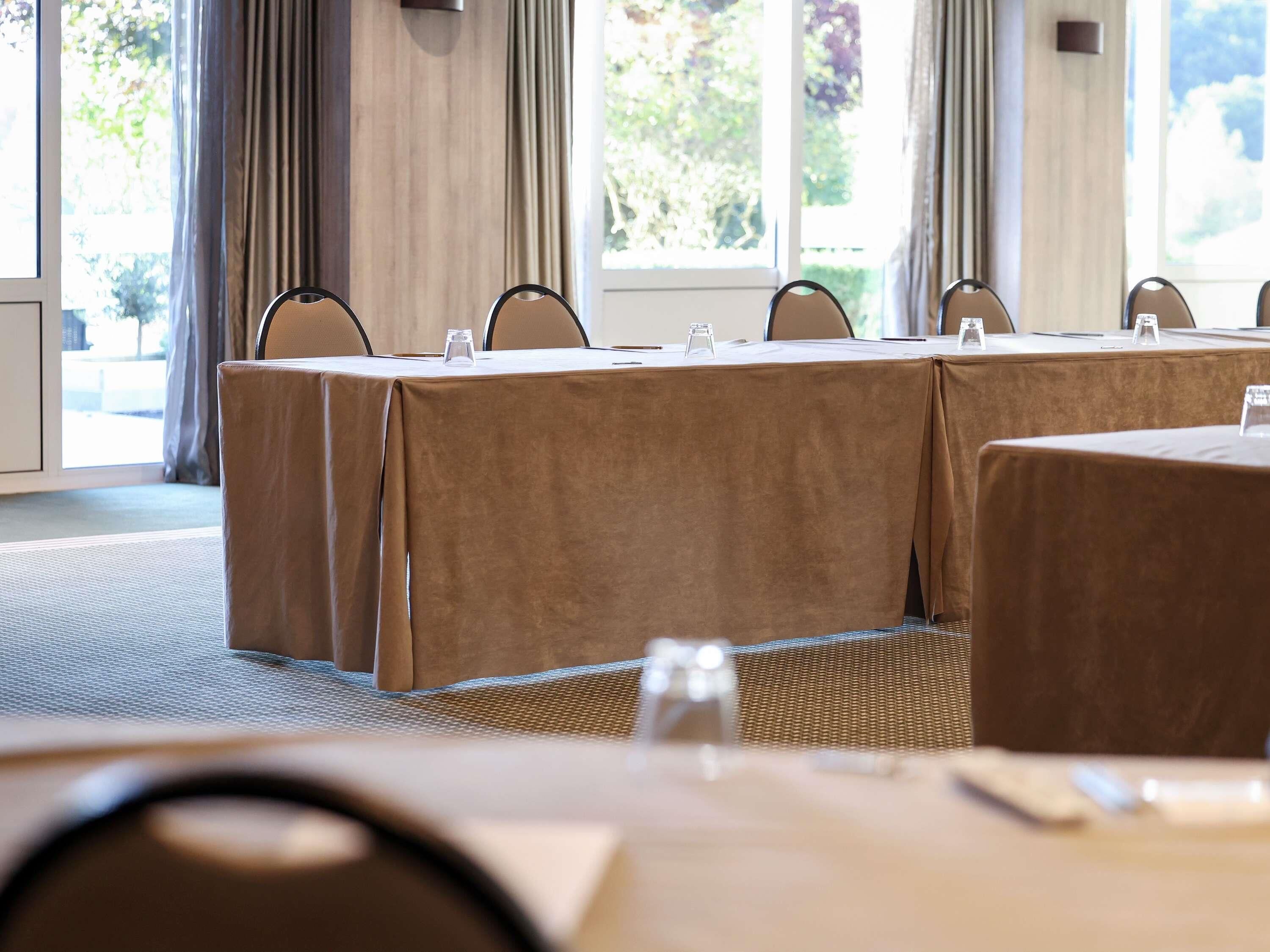 Un salón de conferencias con una larga mesa, sillas y vistas a árboles a través de las ventanas.