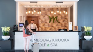 Un comptoir d’accueil en bois, orné d’un grand logo en forme de « M » et d’un écran numérique, se trouve au Kembourg Kikuoka Golf & Spa.