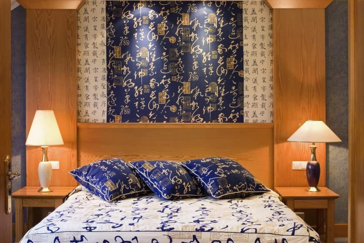 A hotel room with a bed, two bedside tables, and a headboard with a patterned tapestry.