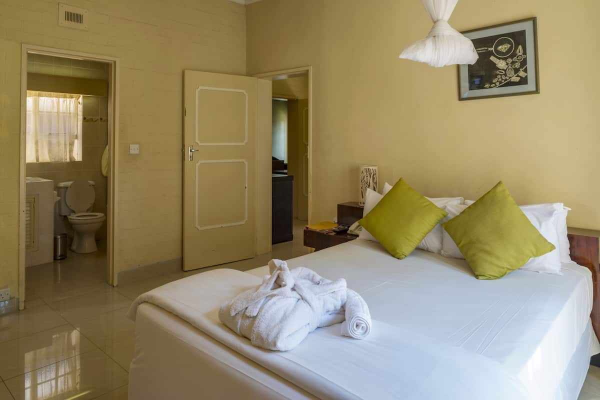 A hotel room with a bed, a bathroom visible through an open door, and a framed picture on the wall.