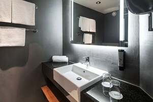 Un baño moderno con un lavamanos blanco, paredes oscuras y un espejo grande.