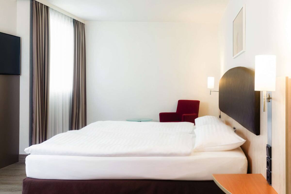 Een hotelkamer met een net opgemaakt bed, een rode stoel, een flatscreen televisie en een lamp.