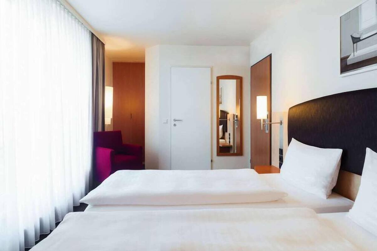 Een hotelkamer met een groot bed, een deur, een spiegel en een raam met gordijnen.