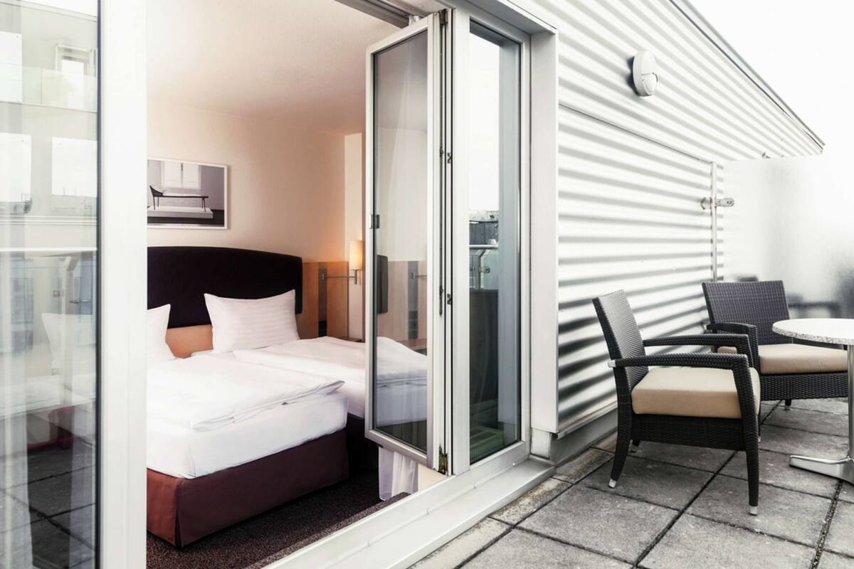 Een hotelkamer met een bed, een schuifglasdeur naar buiten, een kleine tafel en twee stoelen.