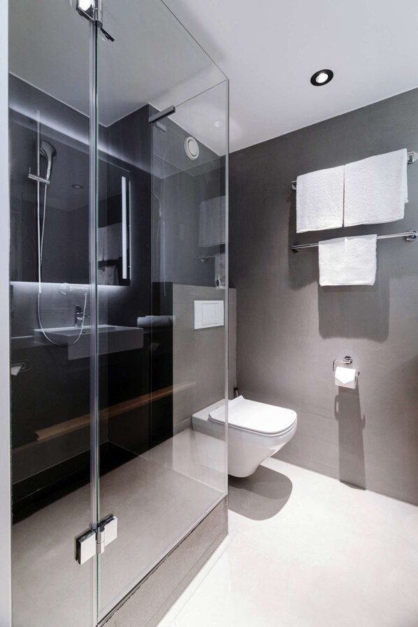A modern bathroom with a glass-enclosed shower, a toilet, and a sink. - IntercityHotel Wien (Vienna)