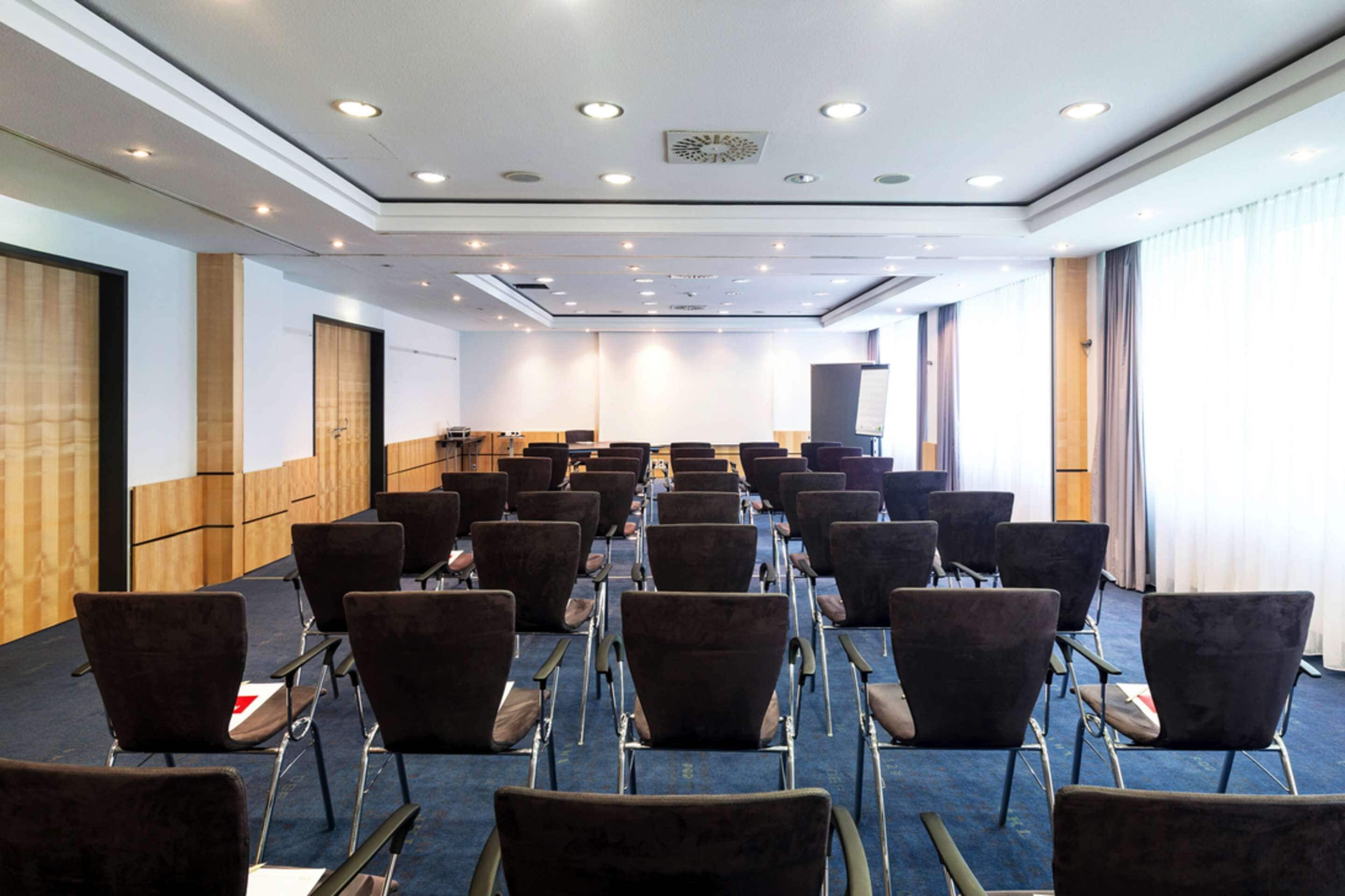 A conference room with rows of chairs, a podium, and a large window with curtains.