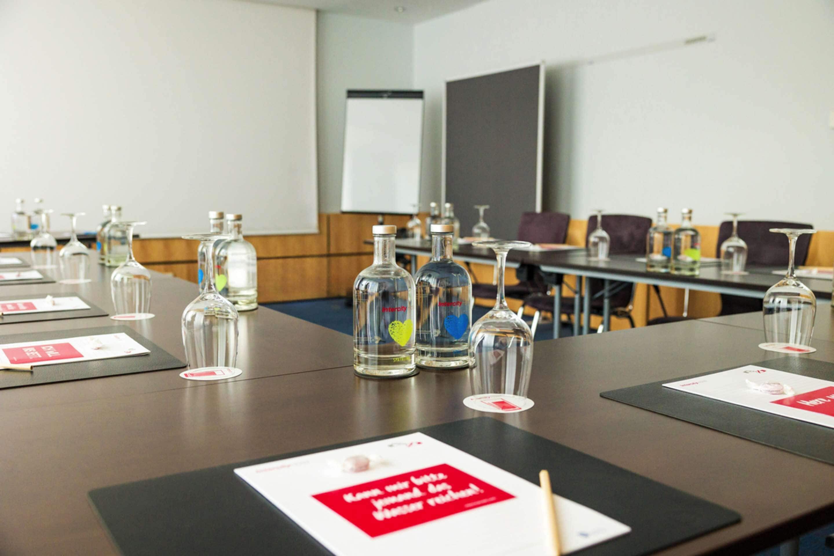 Een vergaderzaal met tafels klaar voor vergaderingen, voorzien van glazen flessen en wijnglazen.