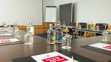Un salón de conferencias con mesas dispuestas para reuniones, equipado con botellas de vidrio y copas de vino.