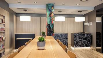 Ein moderner Hotel-Empfangsbereich mit einer langen Rezeption, zwei Pendelleuchten, einer Pflanze im Topf und einer Wand mit Stadtplandesign.
