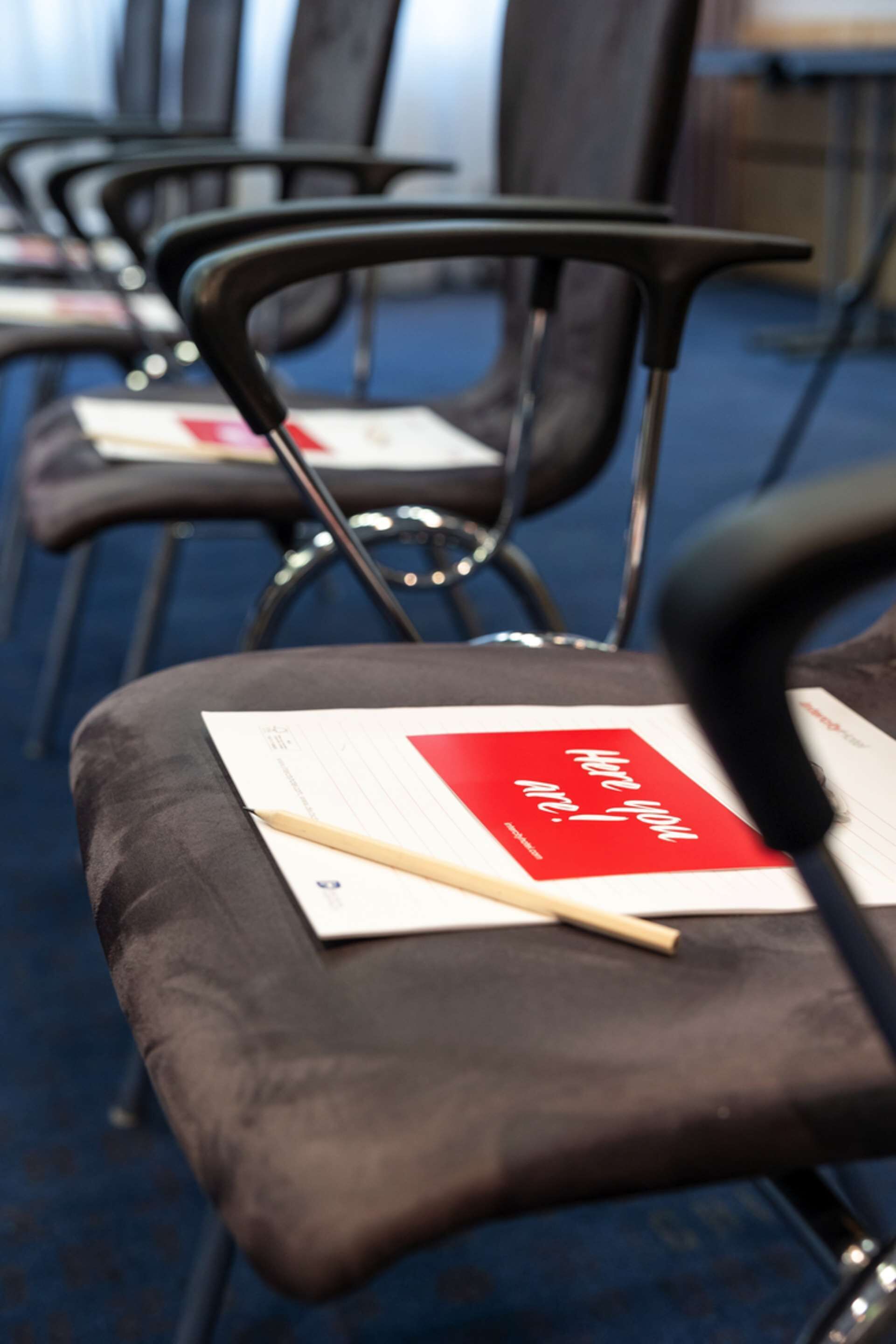 A row of black chairs with a red card and a pencil on one of them.