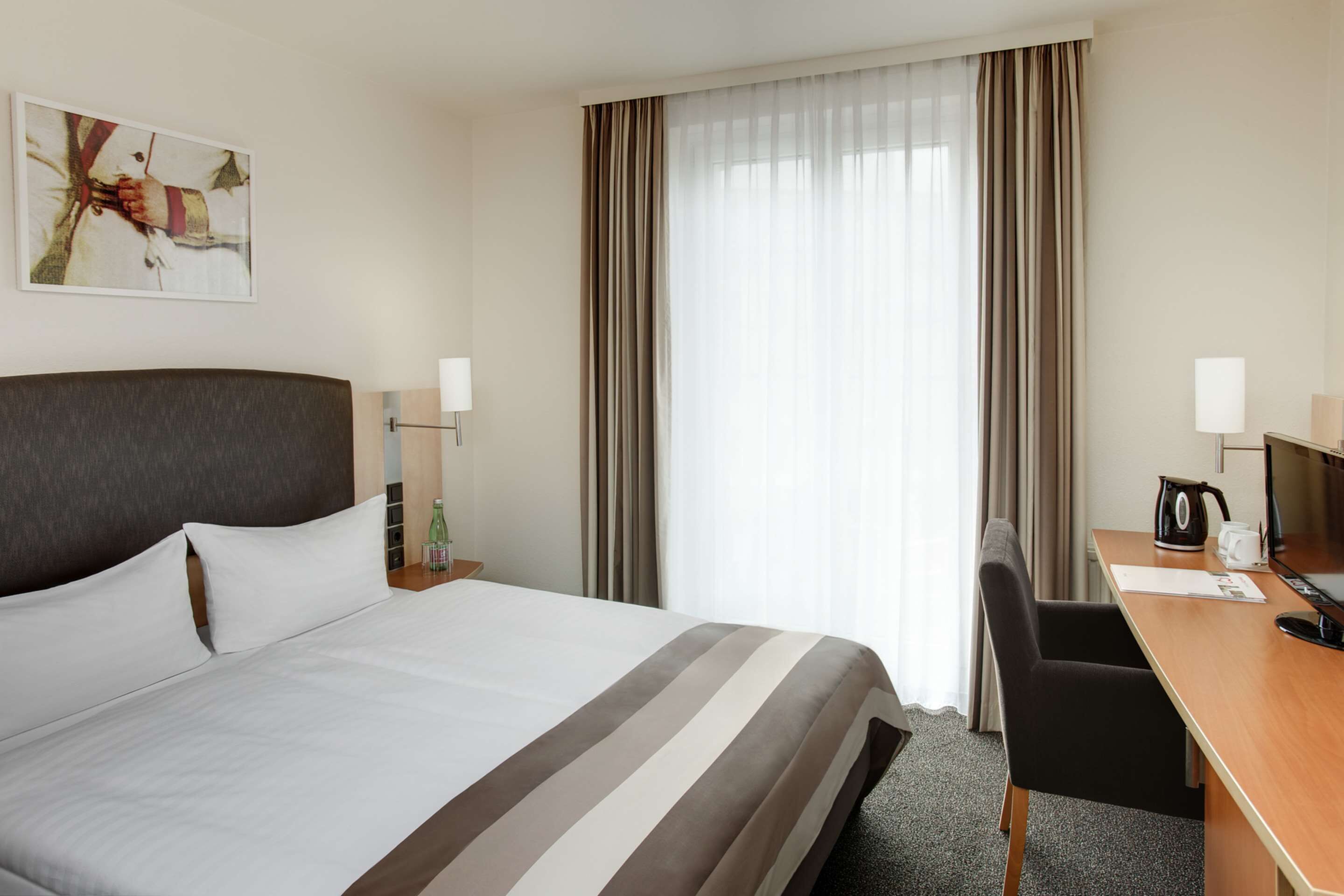 A hotel room with a large bed, a desk with a chair, a coffee maker, and a window with curtains.