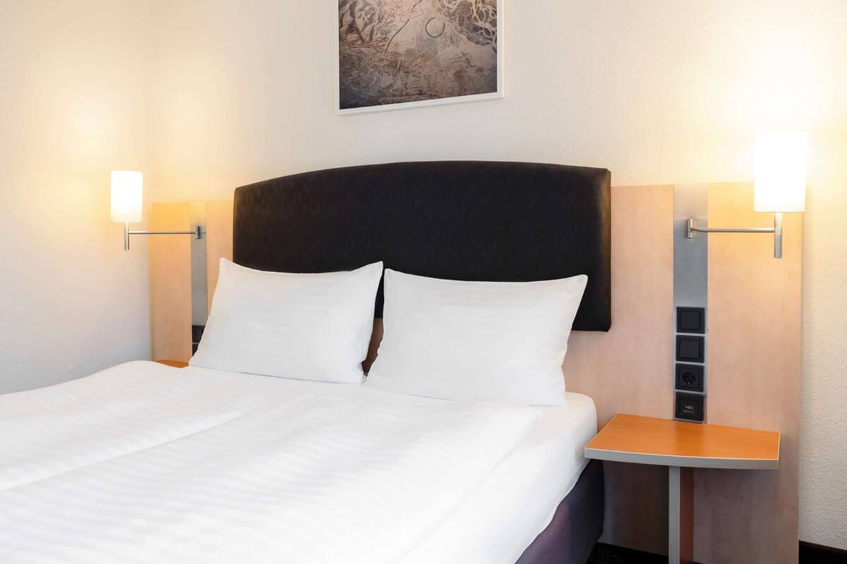 Een hotelkamer met een groot bed, twee nachtkastjes en wandlampen.