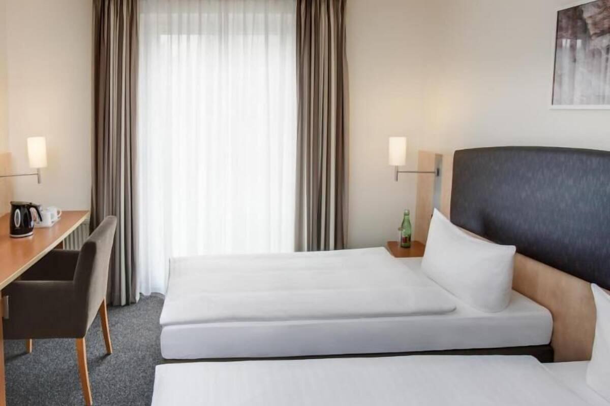 Een hotelkamer met twee bedden, een bureau, een stoel, een lamp en een schilderij aan de muur.
