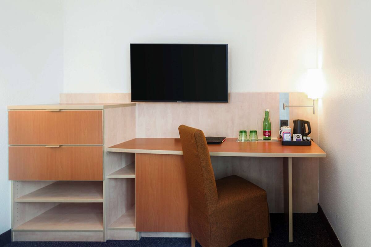 Hotelkamer met een bureau, stoel, flatscreen televisie, koffiezetapparaat en een fles water.