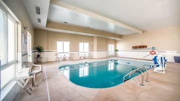 Una piscina interior con agua cristalina, una silla de socorrista y un área de descanso junto a la piscina.