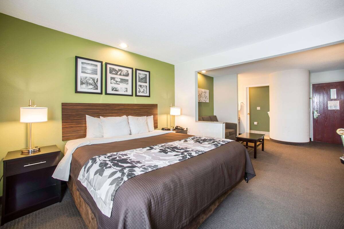 A hotel room with a large bed, two bedside tables with lamps, a desk with a chair, and green walls.