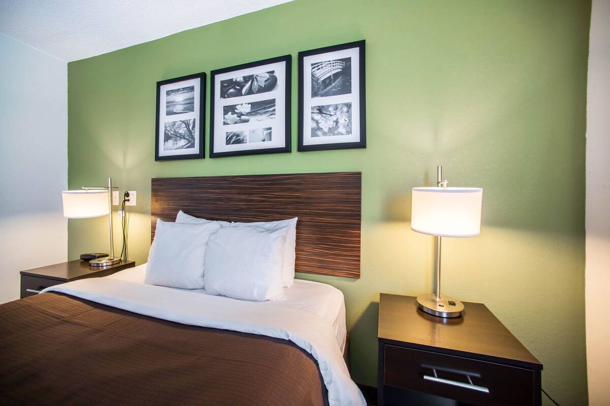 A hotel room with a large bed, two bedside tables, a wooden headboard, and three framed pictures on the wall.