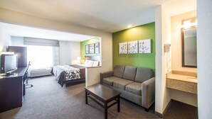Ein Hotelzimmer mit Bett, einer Sitzecke, einem Fernseher, einem Schreibtisch und einem Badezimmer mit Waschbecken und Spiegel.