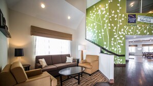 Eine Hotelhalle mit einer Couch, Sesseln, einem Couchtisch, einer Lampe und einer Treppe mit grüner Wand.