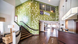 A hotel lobby with a staircase, a reception desk, and a green wall with a plant design. - Sleep Inn Decatur I-72 (Decatur)