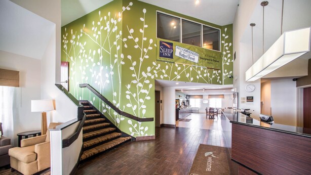 Eine Hotellobby mit Treppe, Empfangstresen und einer grünen Wand mit Pflanzenmuster.