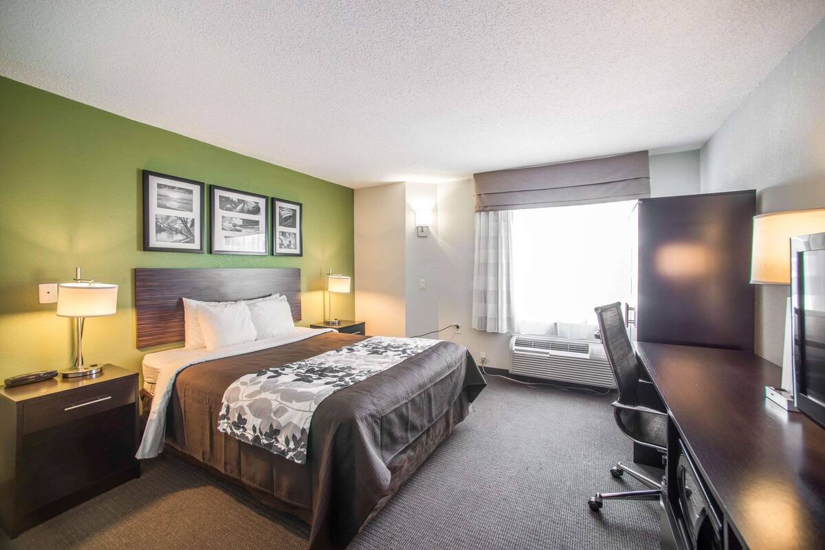 A hotel room with a bed, bedside tables, a desk, and a window with curtains.