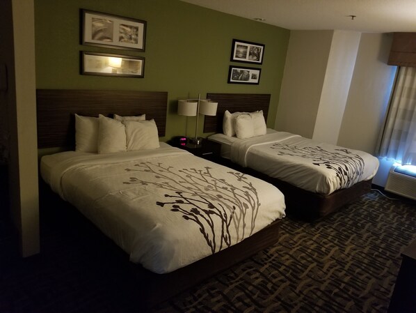 A hotel room with two beds, each with a headboard, a bedside table with a lamp, and framed pictures on the wall. - Sleep Inn Decatur I-72 (Decatur)