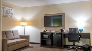 Habitación de hotel con sofá, escritorio con computadora, microondas, refrigerador y televisor de pantalla plana.