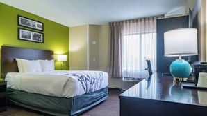 Una habitación de hotel con una cama, un escritorio, una lámpara y un ventanal con cortinas.